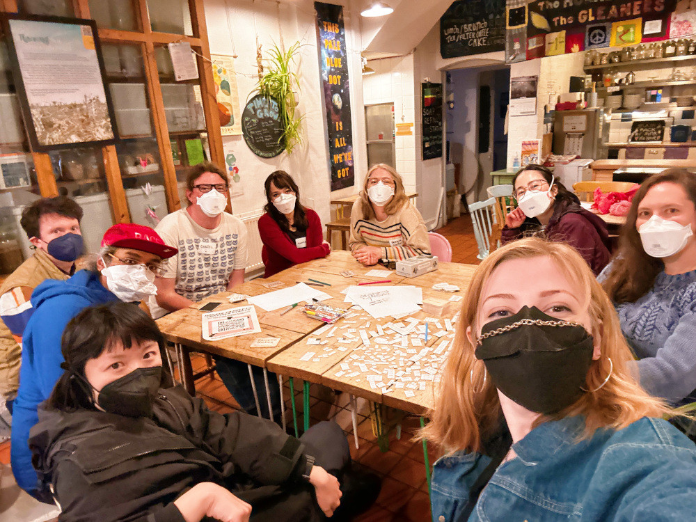 A group of people wearing masks sitting round a large table with craft materials on it